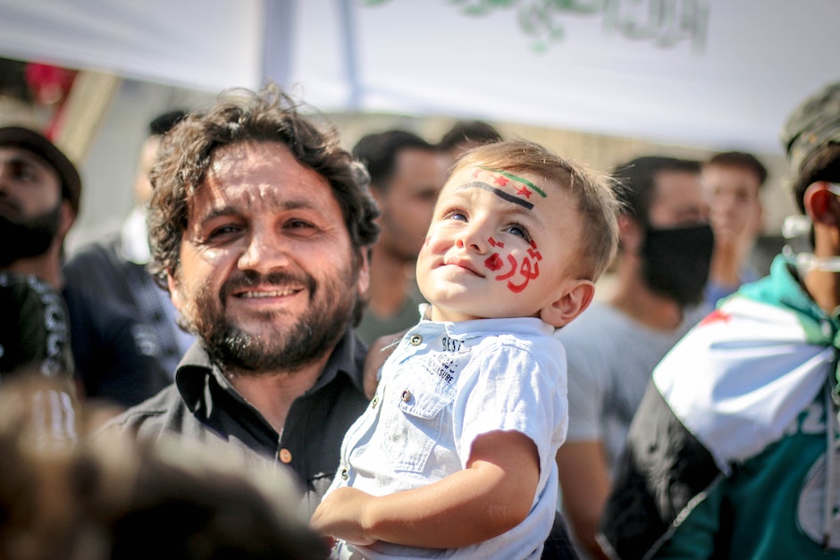 Ethnic bearded man carrying small kid with painted face in crowd of protesting against policy