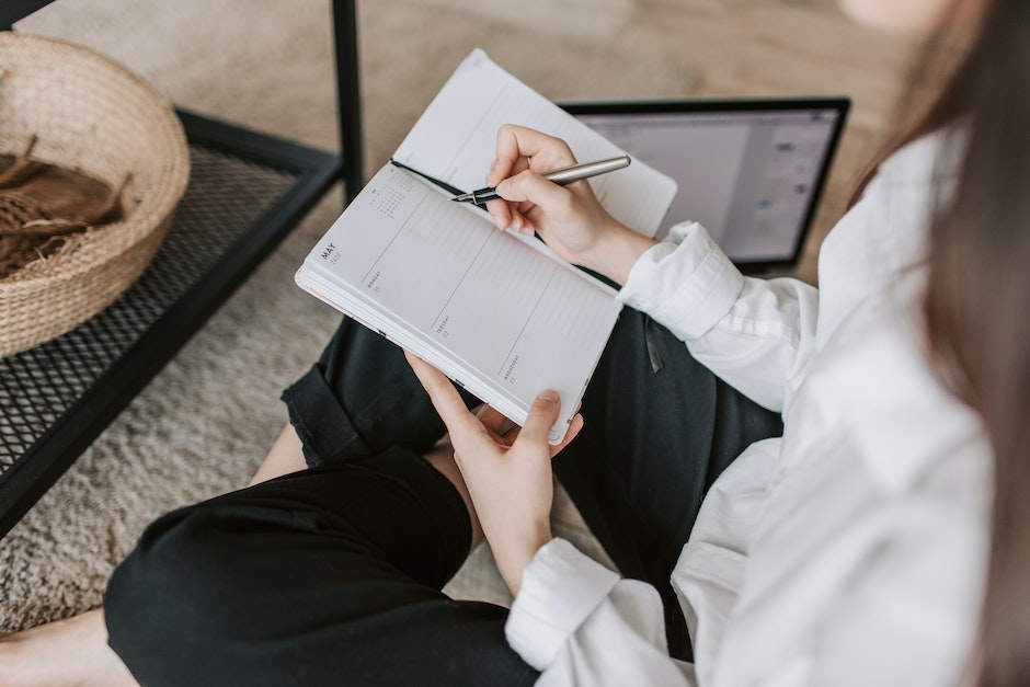 Side view of faceless woman in casual clothes taking notes on notepad while sitting in lotus pose on