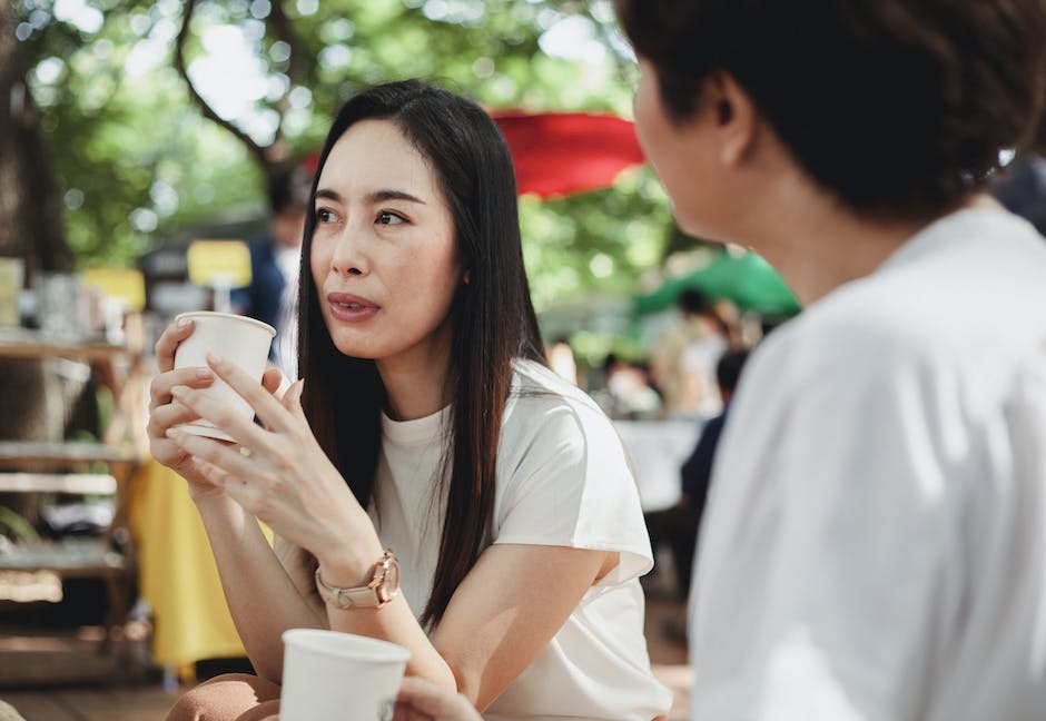 Young Asian girls wearing casual white shirts enjoying fresh aromatic coffee in outdoor cafe