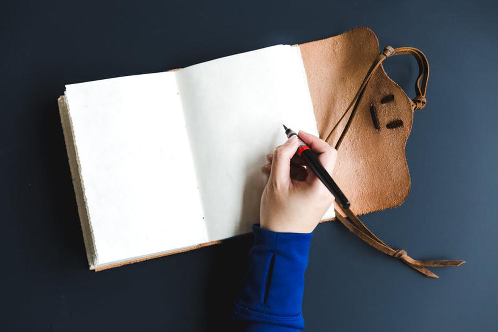 a person writing on a piece of paper with a pencil - blank pages in creative notebook