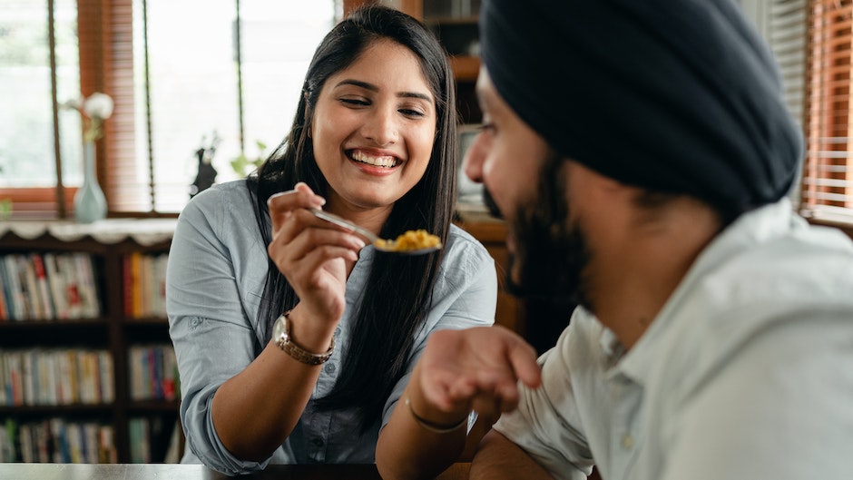 Feliz joven india sonriendo y alimentando a un novio hambriento positivo con delicioso arroz con azafrán