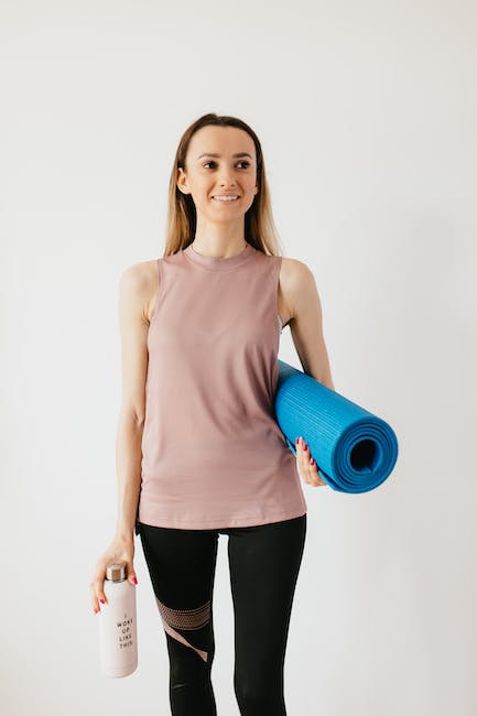 Positive young female athlete in sportswear standing isolated against white wall with blue yoga mat 