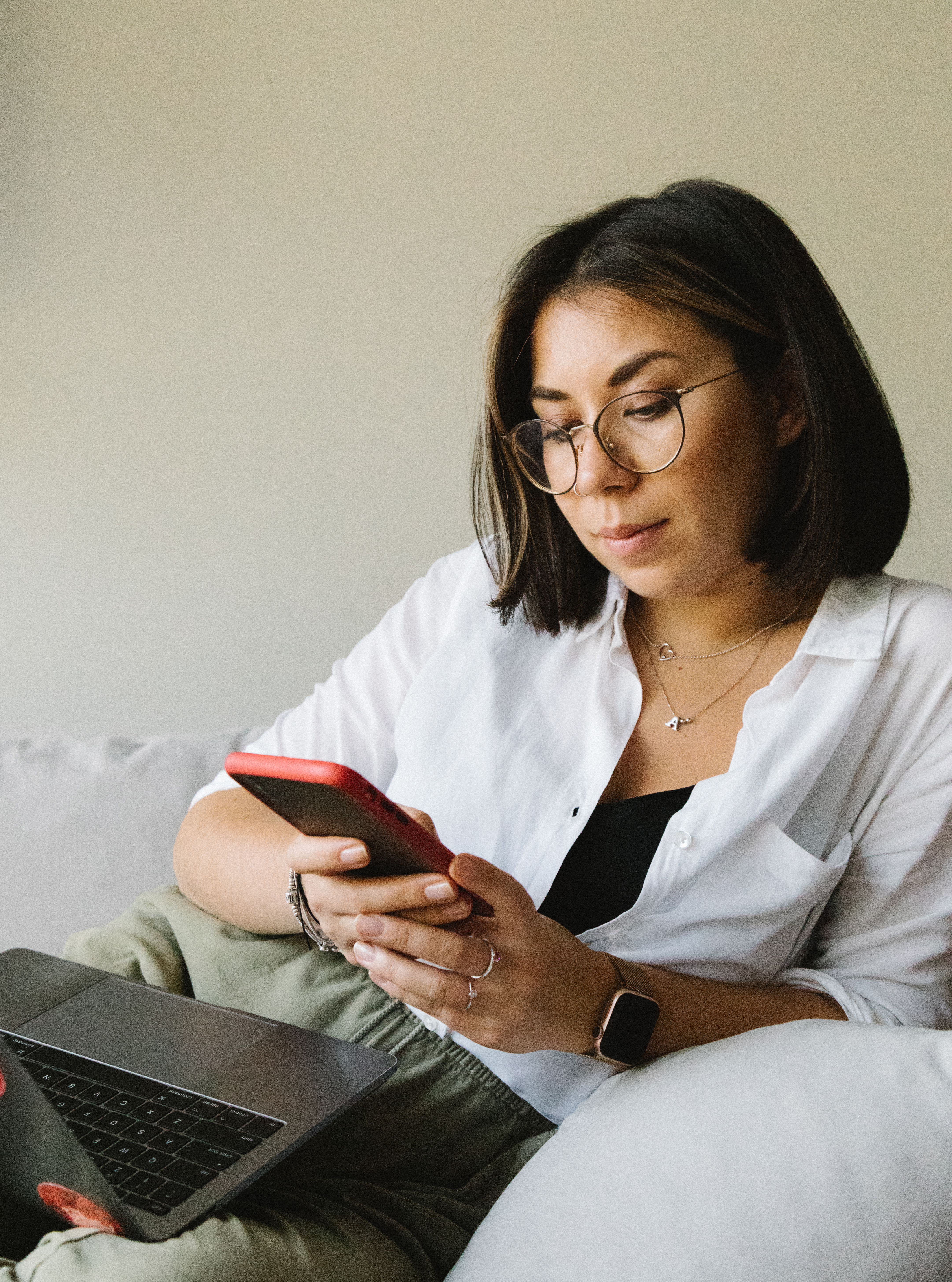 Attractive young female wearing casual outfit and eyeglasses browsing modern mobile phone while lyin